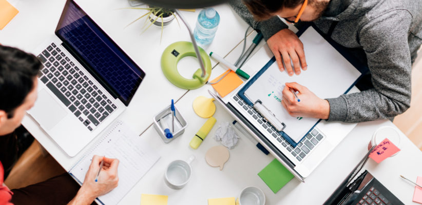 hands working with computers and writing in a notebook